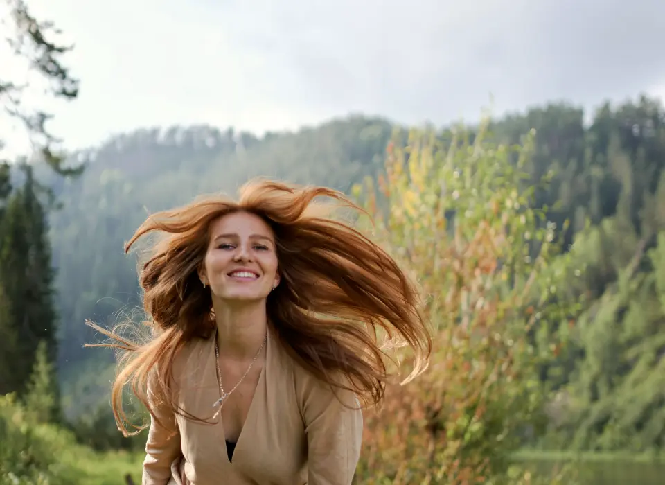 Jolie jeune femme, égérie de la marque cosmatelier. Elle a de longs et beaux cheveux roux resplendissant de santé. Elle marche dans la campagne et en arrière plan on peut voir un lac surplombé d'une forêt de sapin.