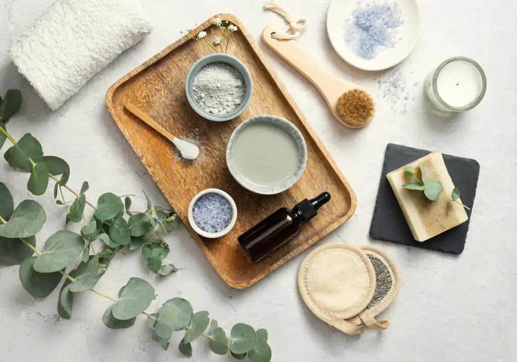 ingredients de cosmétiques naturels sur un plateau en bois. On voit un bol d'argile de l'huile végétale et du feuillage sur un plateau